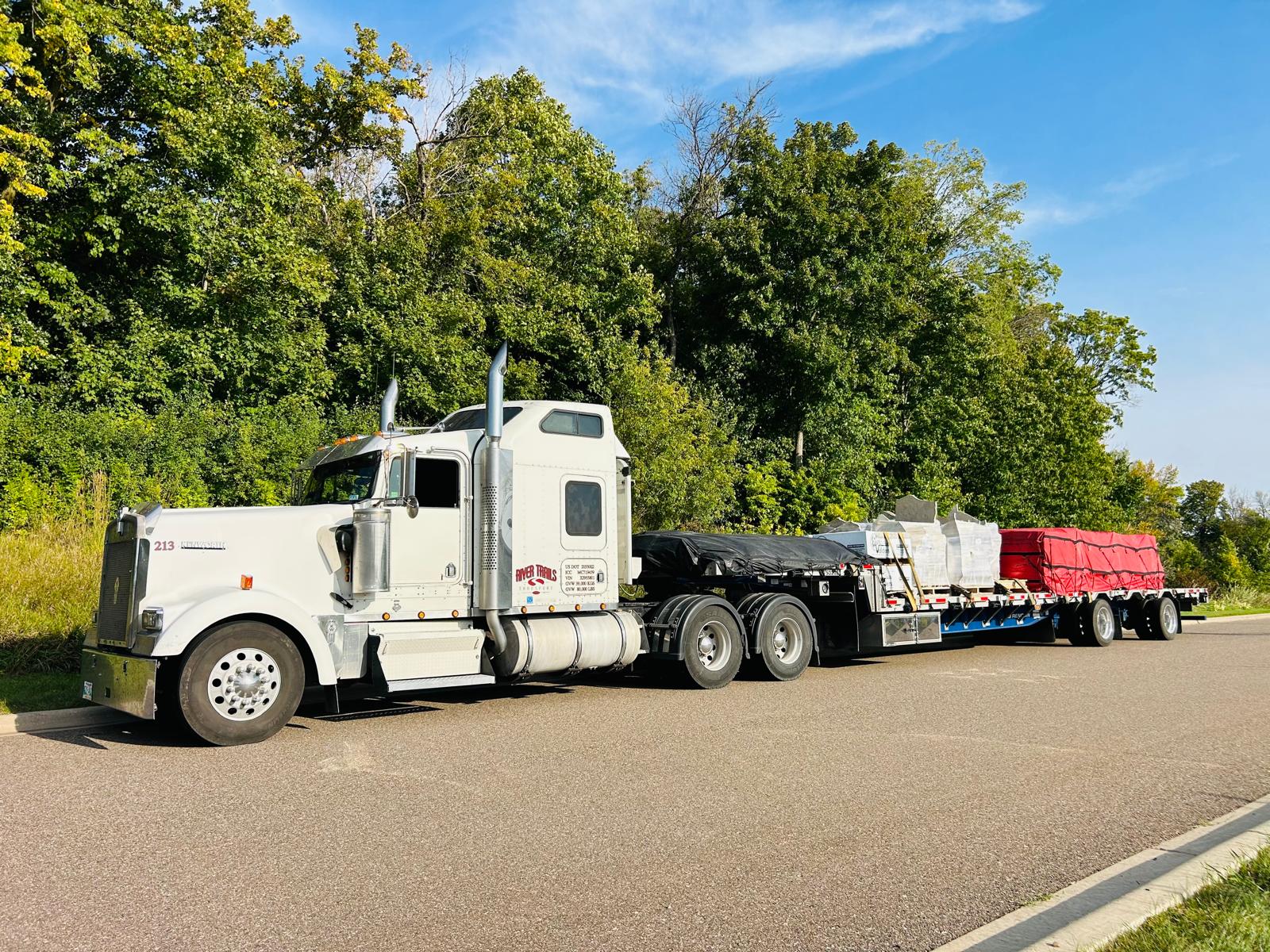River Trails Transport tractor and step-deck trailer parked along a tree-lined country road